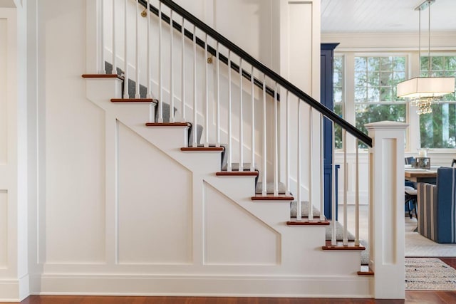 staircase with wood-type flooring, an inviting chandelier, and crown molding