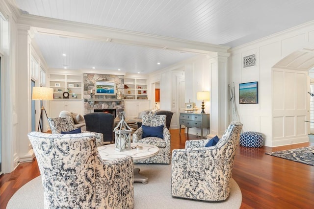 living room with built in shelves, a fireplace, ornamental molding, and dark wood-type flooring