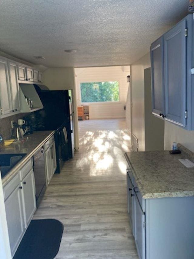 kitchen featuring black dishwasher, a textured ceiling, light wood-type flooring, and sink