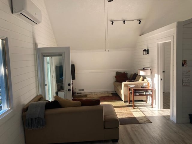 living room with a wall mounted air conditioner, light hardwood / wood-style flooring, and vaulted ceiling