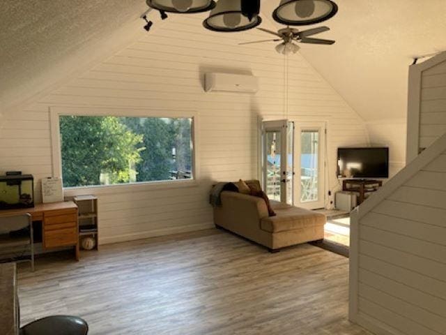 living room with ceiling fan, a wall mounted AC, light hardwood / wood-style floors, a textured ceiling, and vaulted ceiling