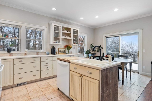 kitchen with white dishwasher, a kitchen island with sink, crown molding, sink, and tile counters