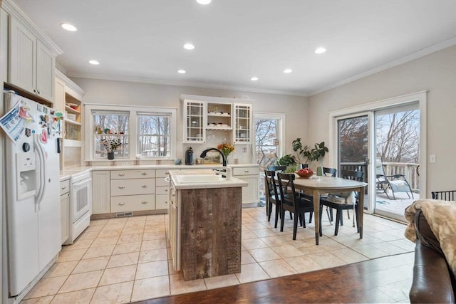 kitchen featuring white appliances, white cabinets, glass insert cabinets, light countertops, and a sink