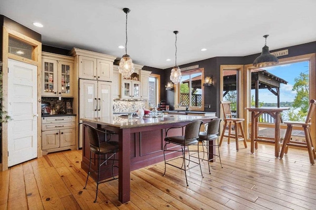 kitchen with a breakfast bar area, light wood-type flooring, decorative light fixtures, and cream cabinetry