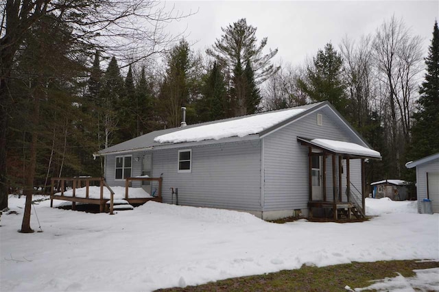 snow covered rear of property with a deck, an outdoor structure, and a garage