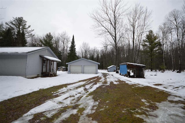 snowy yard with a carport, a garage, and an outbuilding