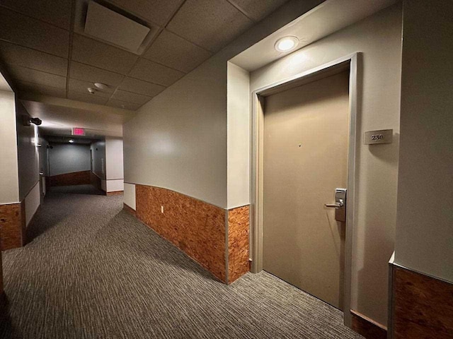 corridor with dark colored carpet and a drop ceiling