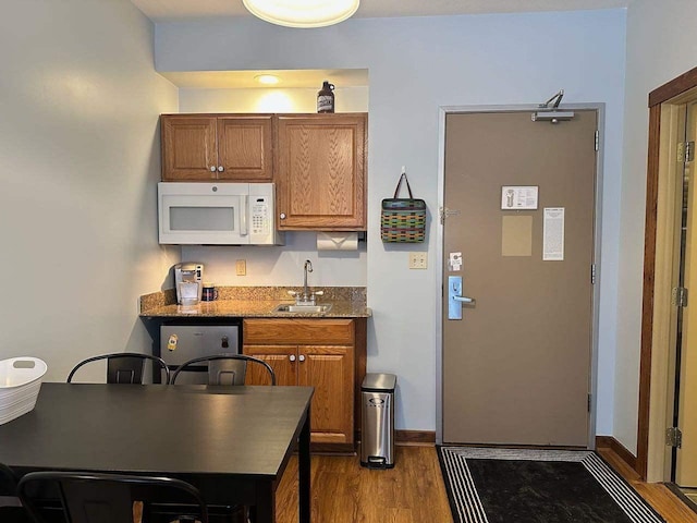 kitchen featuring hardwood / wood-style floors, stone countertops, stainless steel dishwasher, and sink