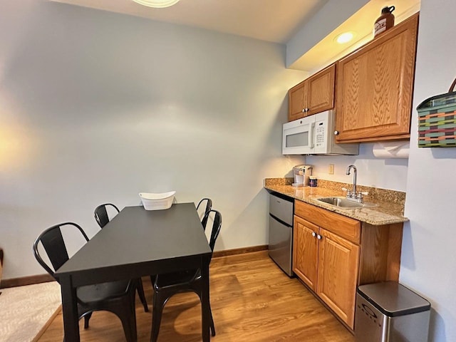 kitchen featuring light stone countertops, light wood-type flooring, dishwasher, and sink