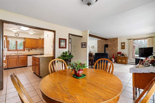 tiled dining room featuring a healthy amount of sunlight, a wood stove, sink, and a baseboard radiator