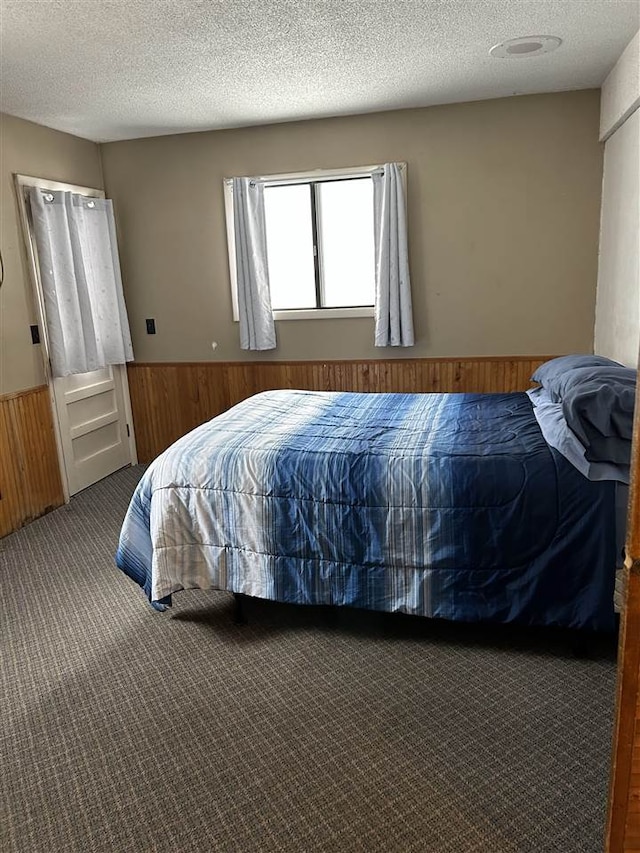 carpeted bedroom featuring wooden walls and a textured ceiling