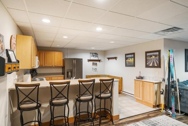 kitchen featuring a breakfast bar, a baseboard heating unit, kitchen peninsula, light hardwood / wood-style floors, and stainless steel fridge with ice dispenser