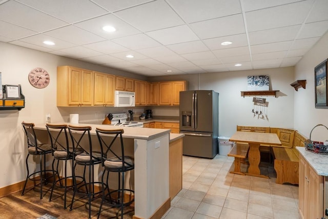 kitchen featuring kitchen peninsula, light tile patterned floors, white appliances, and a breakfast bar area