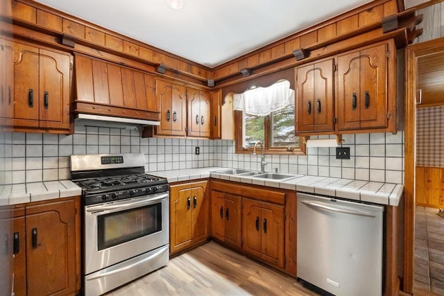 kitchen with tile counters, decorative backsplash, sink, and appliances with stainless steel finishes