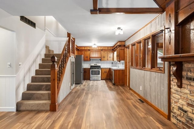 kitchen with light wood-type flooring, stainless steel appliances, and wood walls