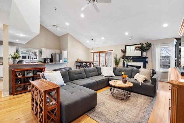 living room featuring a tile fireplace, ceiling fan, sink, high vaulted ceiling, and light wood-type flooring