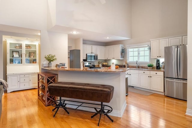 kitchen featuring white cabinets, appliances with stainless steel finishes, a towering ceiling, and light hardwood / wood-style floors