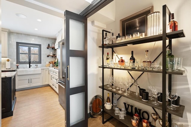 interior space featuring decorative backsplash, light hardwood / wood-style flooring, white cabinets, and sink