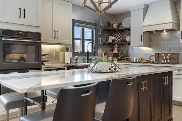 kitchen featuring stainless steel gas cooktop, light stone counters, backsplash, white cabinets, and custom range hood