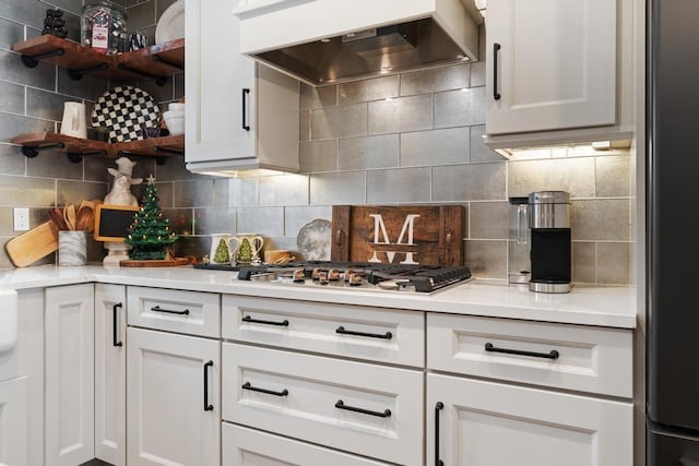 kitchen with wall chimney exhaust hood, white cabinetry, and backsplash