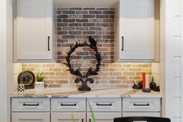 kitchen with white cabinets, light stone counters, and brick wall