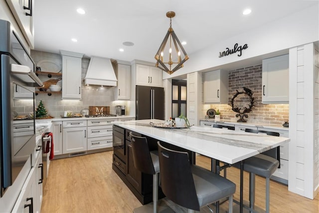 kitchen with white cabinetry, decorative light fixtures, custom range hood, and appliances with stainless steel finishes