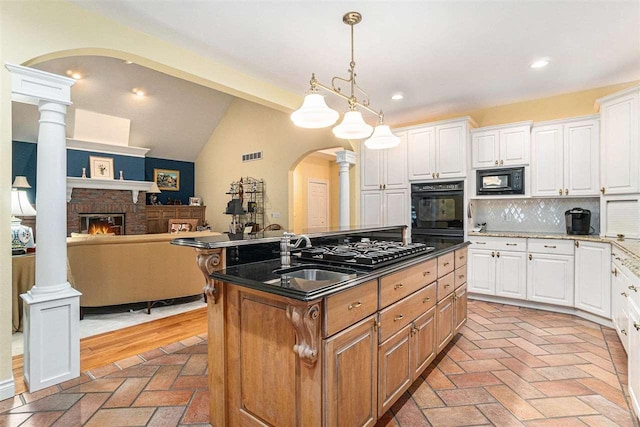 kitchen featuring a kitchen island with sink, white cabinets, black appliances, and a brick fireplace