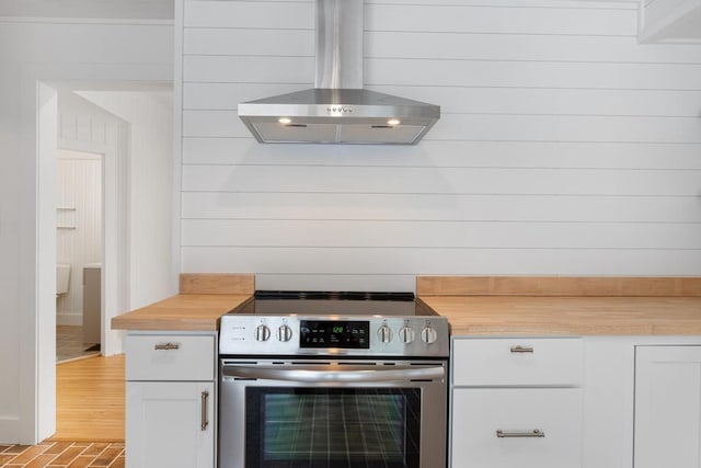 kitchen featuring wood counters, stainless steel electric stove, range hood, white cabinets, and wood walls