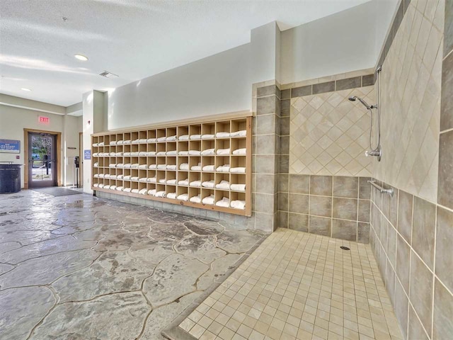 interior space with tiled shower, a textured ceiling, and tile walls