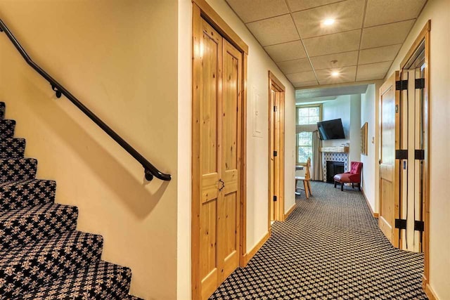 stairway featuring a tile fireplace, a paneled ceiling, and carpet floors