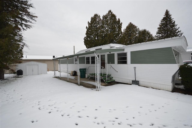 snow covered rear of property featuring a shed