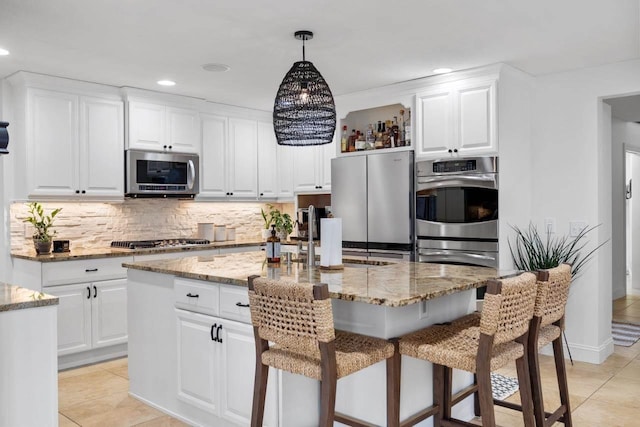 kitchen with appliances with stainless steel finishes, a center island with sink, white cabinetry, and light stone counters