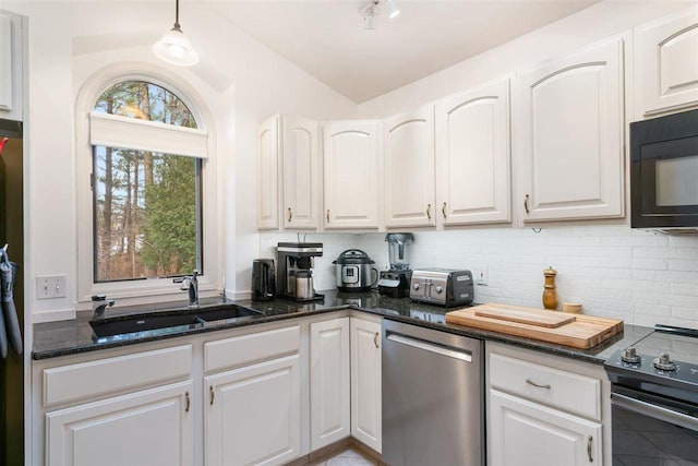 kitchen featuring appliances with stainless steel finishes, sink, dark stone countertops, white cabinets, and hanging light fixtures