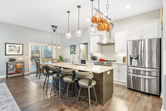 kitchen with wall chimney exhaust hood, stainless steel fridge with ice dispenser, an island with sink, decorative light fixtures, and white cabinets