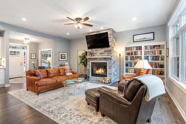 living room with ceiling fan, a stone fireplace, and wood-type flooring