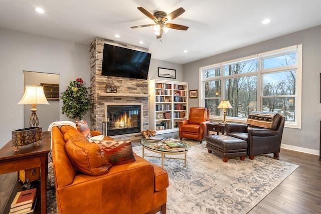 living room featuring ceiling fan, a stone fireplace, and wood-type flooring