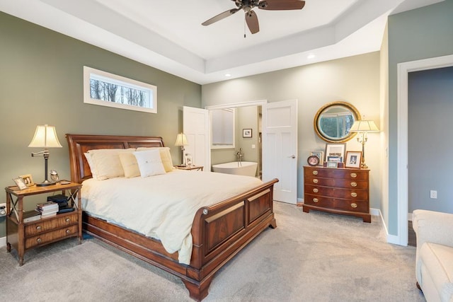 bedroom featuring light colored carpet, ensuite bath, ceiling fan, and a tray ceiling