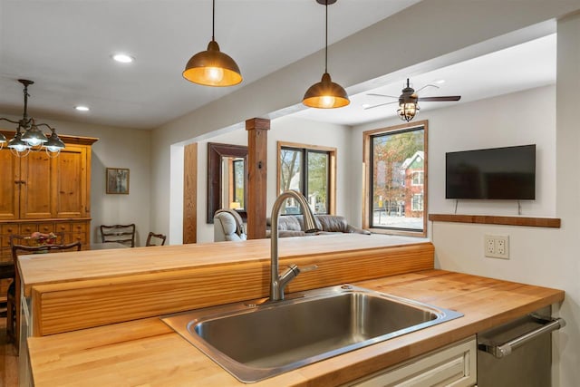 kitchen featuring ceiling fan with notable chandelier, sink, hanging light fixtures, butcher block countertops, and decorative columns