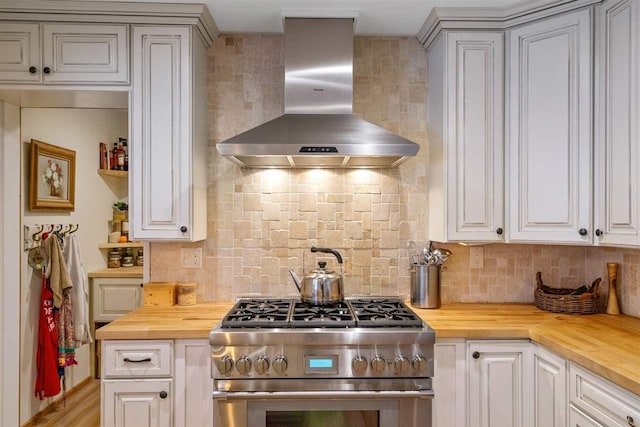 kitchen featuring high end stove, wall chimney exhaust hood, butcher block counters, and backsplash