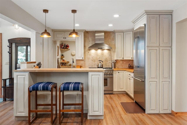 kitchen featuring a kitchen bar, premium appliances, tasteful backsplash, and wall chimney range hood