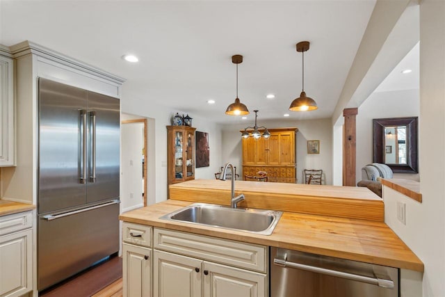 kitchen featuring sink, stainless steel appliances, butcher block countertops, decorative columns, and decorative light fixtures