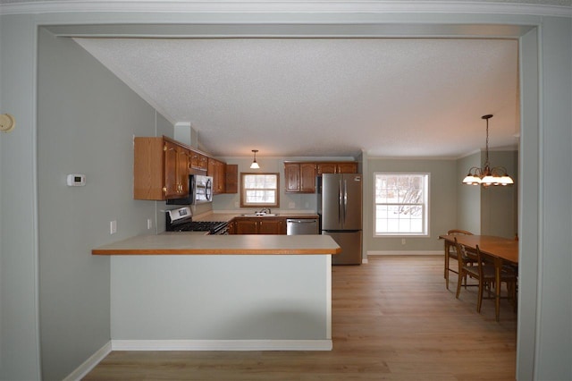 kitchen with pendant lighting, light wood-type flooring, a notable chandelier, kitchen peninsula, and stainless steel appliances