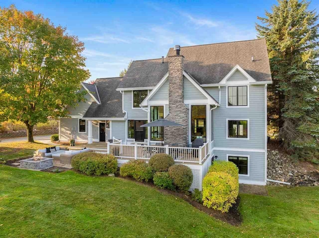 rear view of property featuring a lawn, a deck, and an outdoor fire pit