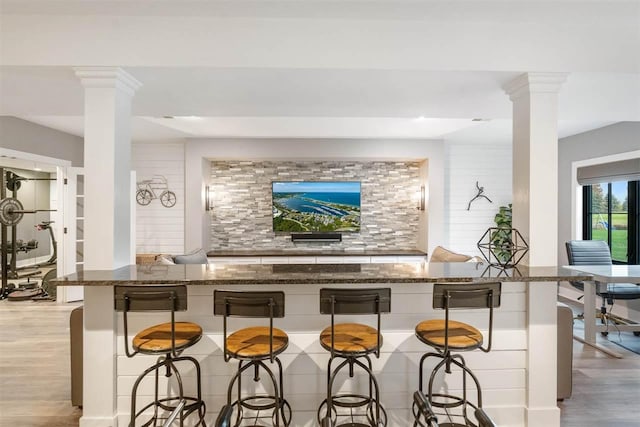 bar featuring decorative columns, backsplash, stone counters, and light hardwood / wood-style flooring