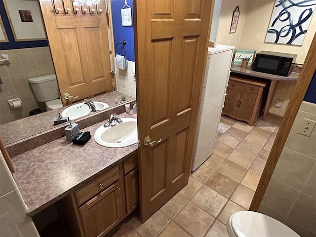 bathroom featuring tile patterned floors, vanity, toilet, and tile walls