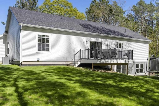 rear view of property with a lawn, a deck, a trampoline, and central air condition unit