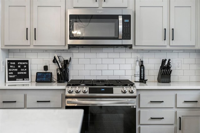 kitchen featuring decorative backsplash, appliances with stainless steel finishes, white cabinetry, and light stone countertops