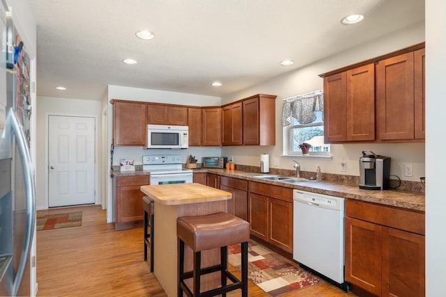 kitchen featuring sink, wood counters, a kitchen breakfast bar, white appliances, and light wood-type flooring