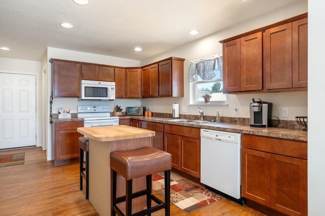 kitchen featuring sink, light hardwood / wood-style flooring, butcher block countertops, white appliances, and a breakfast bar area