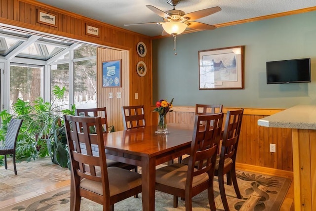 dining area with a textured ceiling, wooden walls, ceiling fan, and crown molding